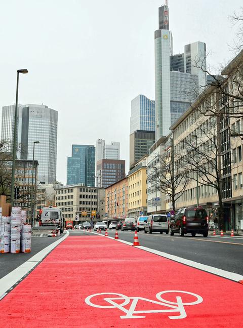 Ein rot markierter Radweg auf einer Straße vor der Frankfurter Skyline.