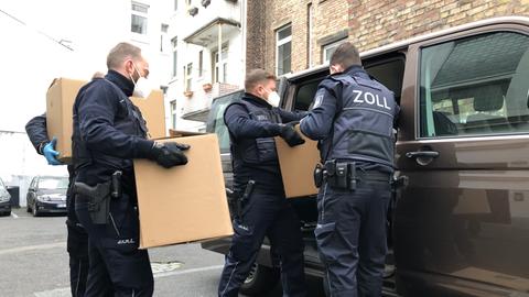 Zollbeamte tragen beschlagnahmte Kisten zu einem Auto. 