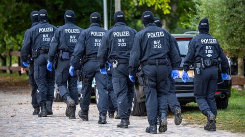 Einsatzkräfte der Polizei führen auf einem Grundstück eine Durchsuchungsaktion durch. 