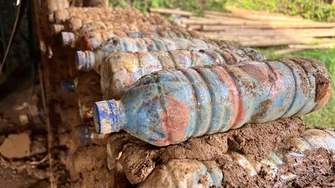 Botol plastik isi ditumpuk di dinding dan disatukan dengan tanah liat.