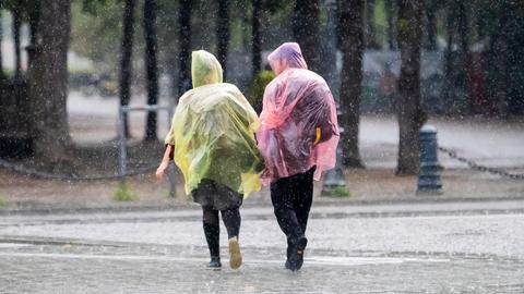 Zwei Passanten in Plastik-Capes gehen durch den Regen.