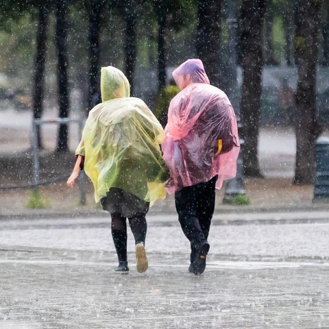 Zwei Passanten in Plastik-Capes gehen durch den Regen.