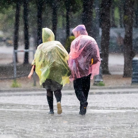 Zwei Passanten in Plastik-Capes gehen durch den Regen.