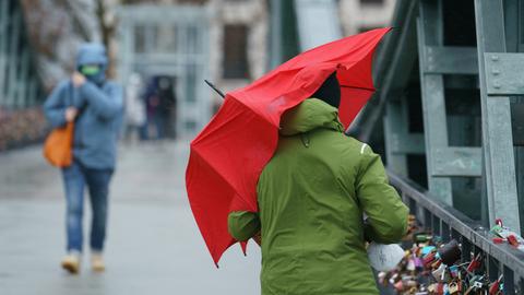 Eine Person schützt sich auf dem Eisernen Steg mit einem Schirm gegen den Regen. 