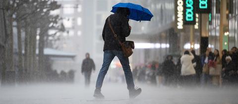 Mann geht mit Schirm bei Regen in einer Fußgängerzone
