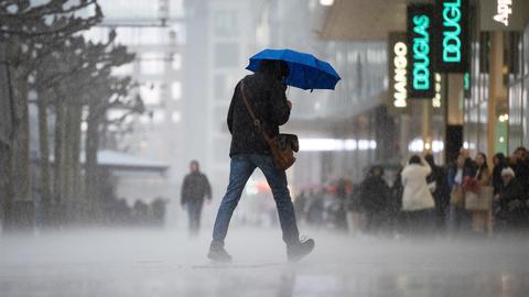 Mann geht mit Schirm bei Regen in einer Fußgängerzone