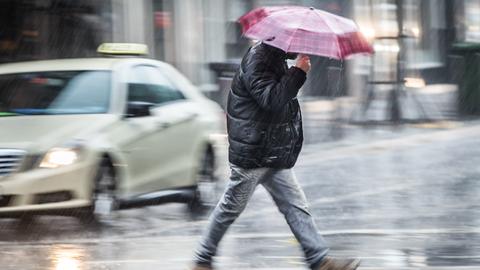 Ein Mann mit Regenschirm beeilt sich, bei strömenden Regen eine Straße in der Frankfurter Innenstadt zu überqueren.