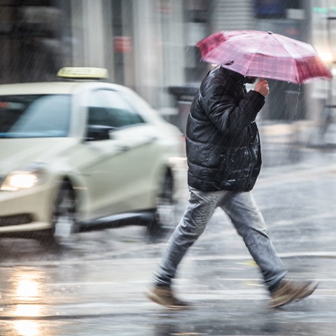 Ein Mann mit Regenschirm beeilt sich, bei strömenden Regen eine Straße in der Frankfurter Innenstadt zu überqueren.