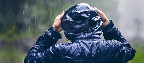 Mensch mit Regenjacke zieht sich im Regen die Kapuze über