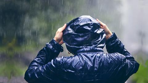 Mann mit Regenjacke zieht im Regen seine Kapuze an