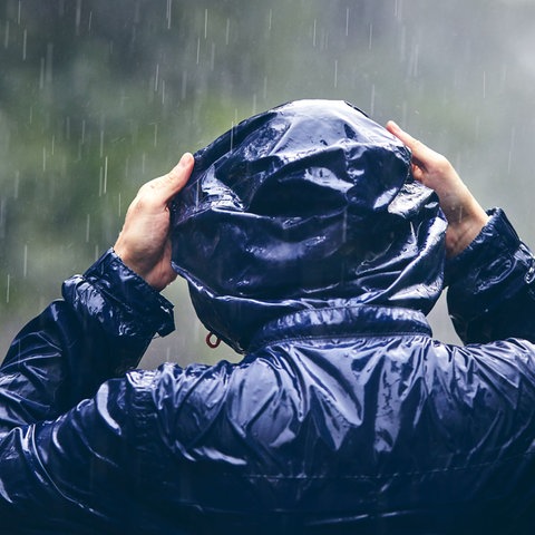 Mensch mit Regenjacke zieht sich im Regen die Kapuze über