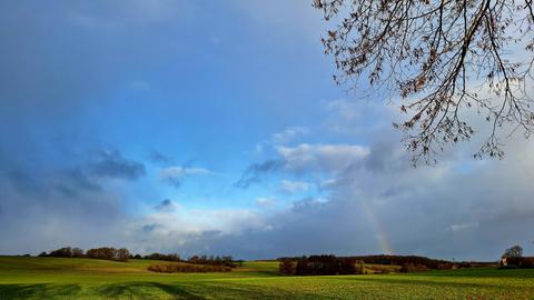 Kleiner Regenbogen über Feld mit blauem Himmel