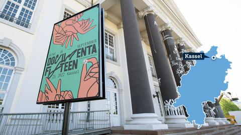 Foto: Ein Schild mit dem aktuellen, farbenfrohen Plakat der documenta 2022 steht vor dem Museum Fridericianum. Vor allem die Säulen des Eingangsportals sind zu sehen. Im Foto ist rechts eine kleine, blaue Hessenkarte mit der Stadt Kassel verortet. 