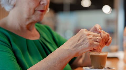 Eine Rentnerin sitzt im Café und trinkt einen Kaffee. 