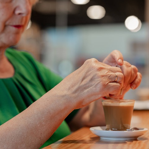 Eine Rentnerin sitzt im Café und trinkt einen Kaffee. 