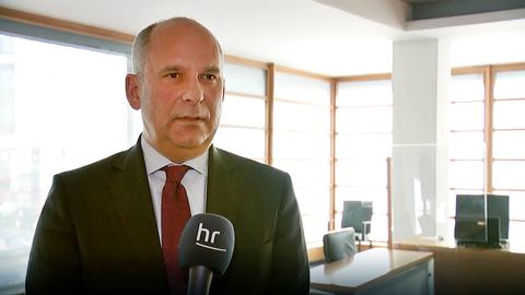 Roman Poseck steht in einem Büro und spricht in ein Mikrofon.