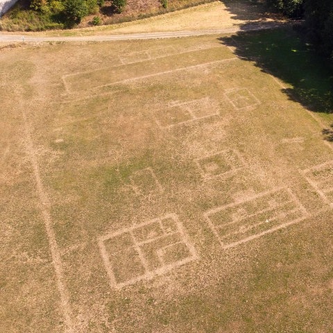 Ein Luftbild eines Feldes, auf welchem grundrissähnliche Zeichnungen aus dem Erdreich durchschimmern.