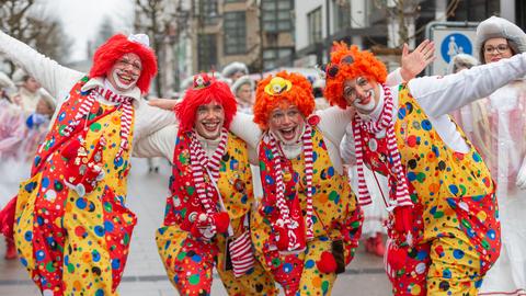 Vier Personen in Clownskostümen stehen lachend auf einer Straße.
