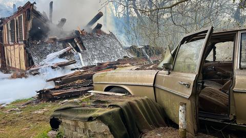 Altes Auto vor ausgebranntem Haus mit Löschschaum
