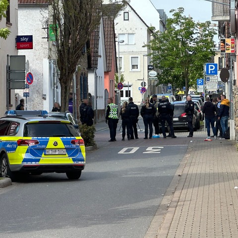 Polizei und Zeugen stehen auf einer abgesperrten Straße am Tatort in Rüsselsheim.
