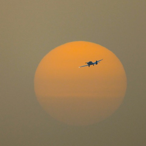 Einmotoriges Flugzeug im Sonnenuntergang, Himmel leuchtet orange-gelb