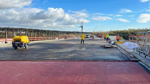 Straßenbaustelle mit "rohem" Boden, Baustellengeräte und -werkzeuge und Arbeiter in gelb-orangener Arbeitskleidung.