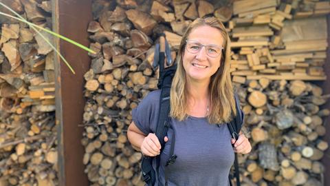 Sandra Köhler mit Rucksack vor einem Holzstapel