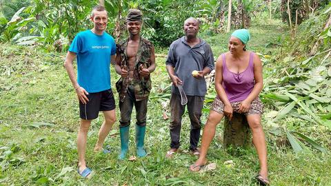 Sascha Gramm steht neben drei einheimischen Menschen auf einer Plantage in São Tomé.