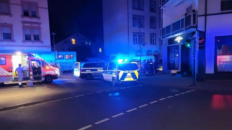 Ein Krankenwagen und zwei Polizeifahrzeuge halten auf einer nachtdunklen Straße, die nur vom Licht der Straßenlampen erleuchtet wird.