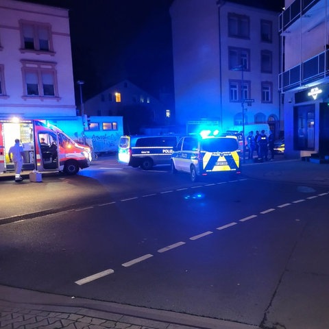 Ein Krankenwagen und zwei Polizeifahrzeuge halten auf einer nachtdunklen Straße, die nur vom Licht der Straßenlampen erleuchtet wird.