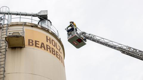 Eine Einsatzkraft der Feuerwehr steht in der Gondel eines Hubarms und wird an das Obere eines Silos herangefahren.