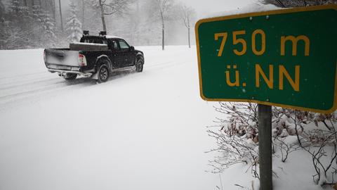 Geschlossene Schneedecke auf dem Hoherodskopf im Vogelsberg, ein Pick-up fährt an einem Schild mit Aufschrift (750 m ü. NN) vorbei