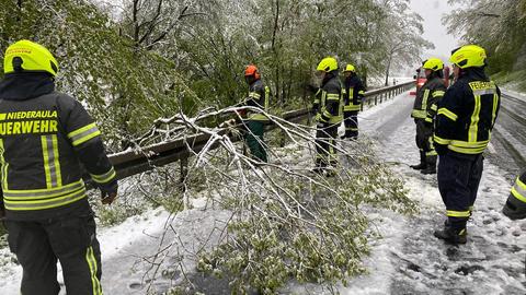 Einsatzkräfte auf einer verschneiten Straße mit abgebrochenen Ästen