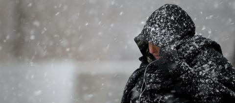 Eine Passantin zieht sich bei Schneefall die Kapuze über den Kopf