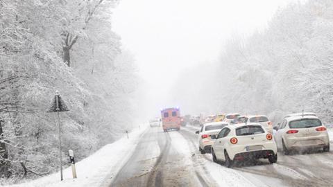 Im Stau stehende Autos auf einer schneebedeckten Straße im Wald, davor ein Rettungswagen.
