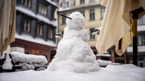 Ein kleiner Schneemann mit einer Nase aus einem Bleistift und Armen aus Löffeln steht auf dem Tisch im verschneiten Außenbereich eines Cafes in der neuen Frankfurter Altstadt. 