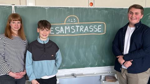 Vertrauenslehrerin Nina Illmer, die Schüler Alexander Mainka und Benjamin Bähre stehen vor einer Tafel. Dort ist mit Kreide der Schriftzug "Sesamstraße" aufgemalt.