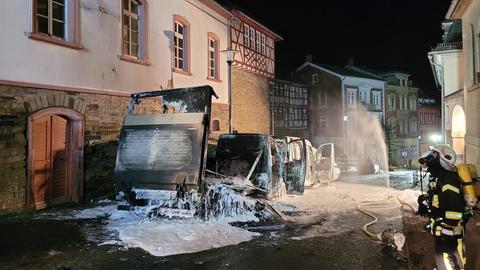Mehrere ausgebrannte Fahrzeuge stehen in einer Straße in einer Altstadt, daneben ein Feuerwehrmann.