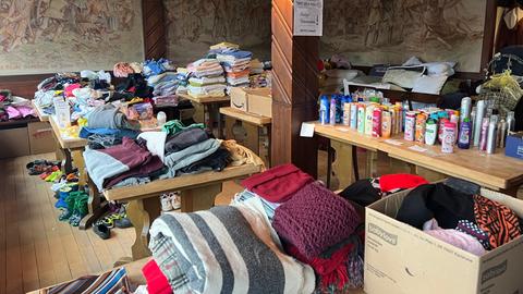 Der Raum mit den gesammelten und gestapelten Spenden - vor allem Kleider und Drogerieartikel liegen auf Tischen.
