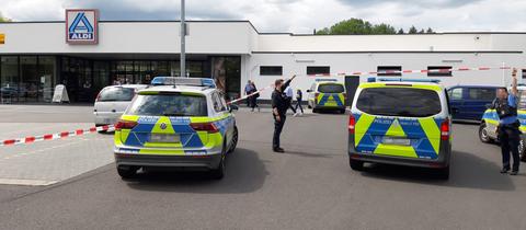 Polizeiautos, Polizisten und ein Absperrband auf einem Parkplatz eines Lebensmitteldiscounters, der im Hintergrund zu sehen ist.