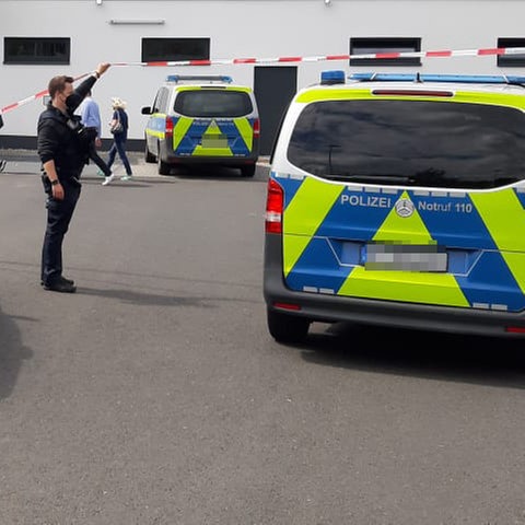 Polizeiautos, Polizisten und ein Absperrband auf einem Parkplatz eines Lebensmitteldiscounters, der im Hintergrund zu sehen ist.