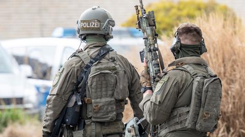 Zwei Beamte eines Spezialeinsatzkommandos (SEK) der Frankfurter Polizei in voller Ausrüstung von hinten. Eine Person trägt einen Helm, auf dem "Polizei" steht, die andere ist ohne Helm und trägt ein großes Maschinengewehr. 