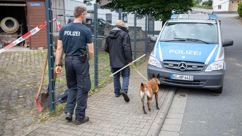 Das Bild zeigt einen SEK-Einsatz auf einem Hof mit Fachwerkhaus. Polizisten führen einen Spürhund über das Gelände.