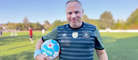 Portrait Jörn Perske. Er schaut auf einem Fußballfeld stehend in die Kamera und hat einen Fußball unterm Arm.