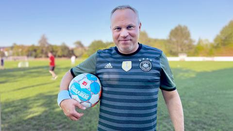 Portrait Jörn Perske. Er schaut auf einem Fußballfeld stehend in die Kamera und hat einen Fußball unterm Arm.