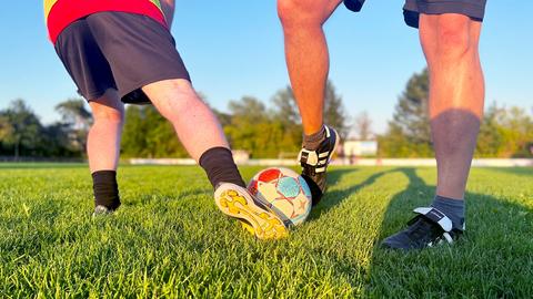 Zwei Beinpaare, die in der Abendsonne mit einem Fußball spielen.