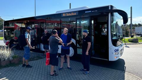 Männer mit Taschen stehen vor einem Bus mit der Aufschrift "Schulbus"