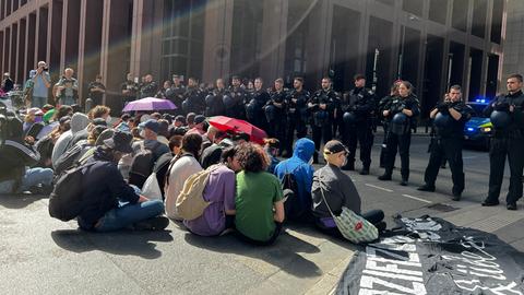 Menschen sitzen auf Straße, davor stehen Polizistinnen und Polizisten