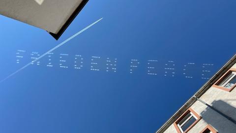 "Frieden - Peace" steht in weißen Großbuchstaben am blauen Himmel