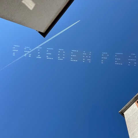 "Frieden - Peace" steht in weißen Großbuchstaben am blauen Himmel